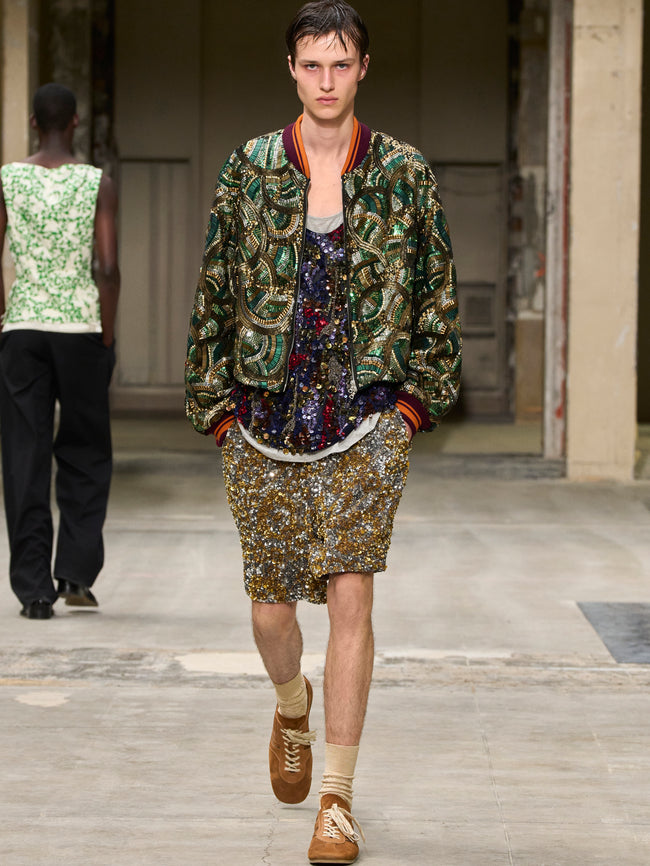 Model walking on a runway wearing a patterned outfit with a green jacket and floral skirt. - Dries Van Noten