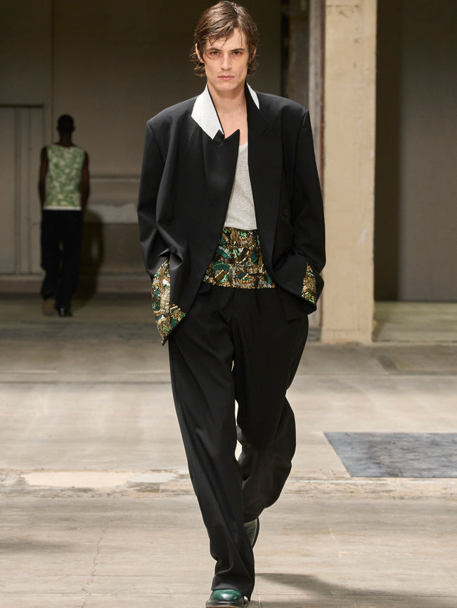 Man walking on a runway wearing a black suit with floral waistcoat and white shirt. - Dries Van Noten