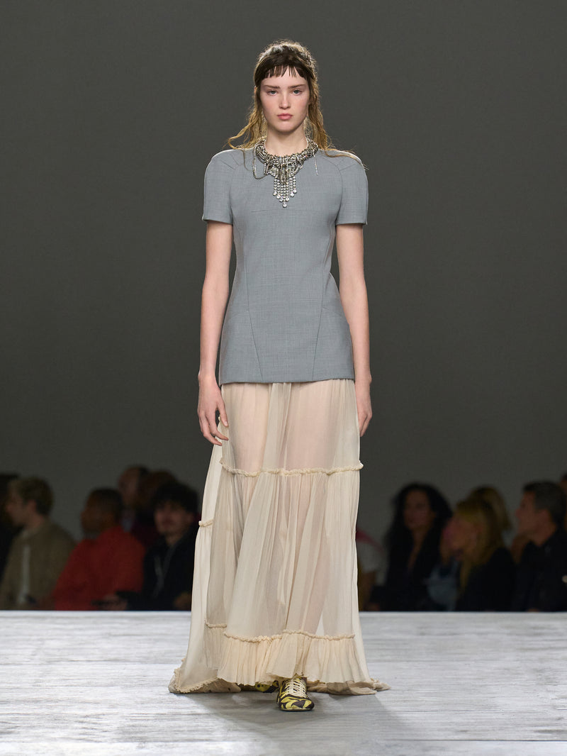 Model on a fashion runway wearing a gray top and beige layered skirt.