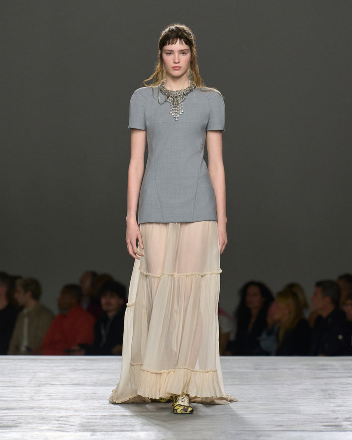 Model on a fashion runway wearing a gray top and beige layered skirt.