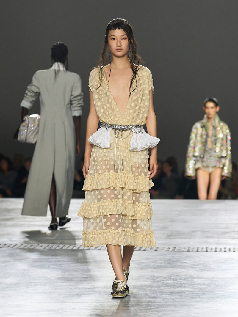 Model walking on a runway wearing a layered, patterned dress.