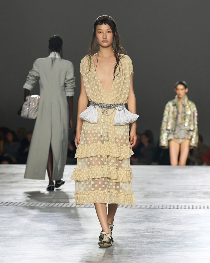 Model walking on a runway wearing a layered, patterned dress.