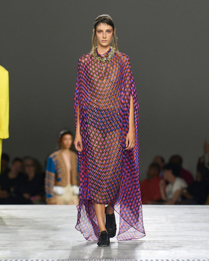 Model walking on a runway wearing a colorful geometric dress.