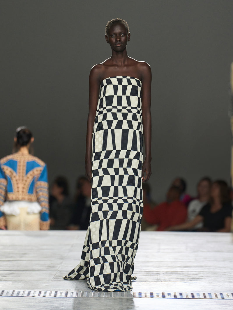 Model wearing a strapless black and white checkered dress on a runway.
