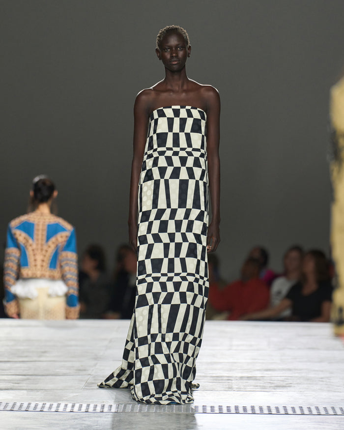 Model wearing a strapless black and white checkered dress on a runway.