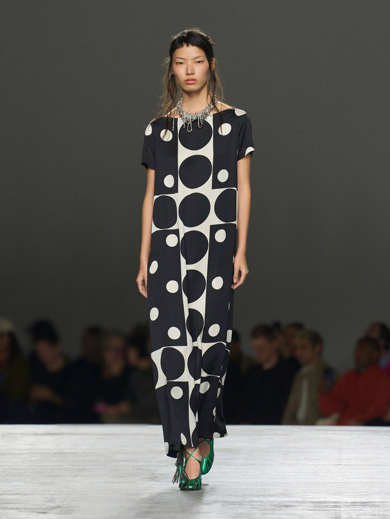 Model wearing a black and white polka dot dress on a runway with an audience.