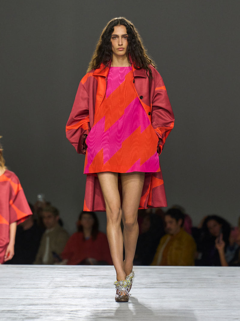Model walking on a runway wearing a colorful outfit with geometric patterns.