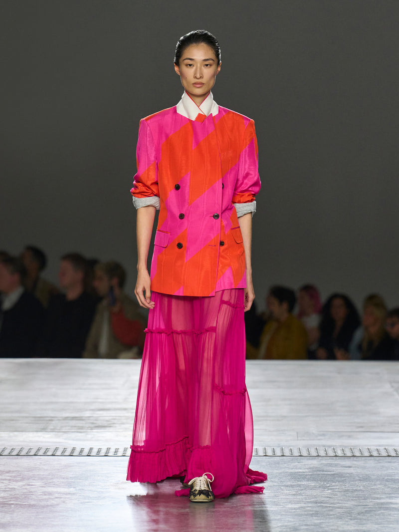 Model walking on a runway wearing a vibrant outfit with geometric patterns.