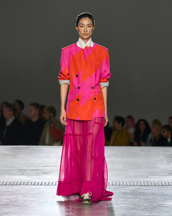 Model walking on a runway wearing a vibrant outfit with geometric patterns.