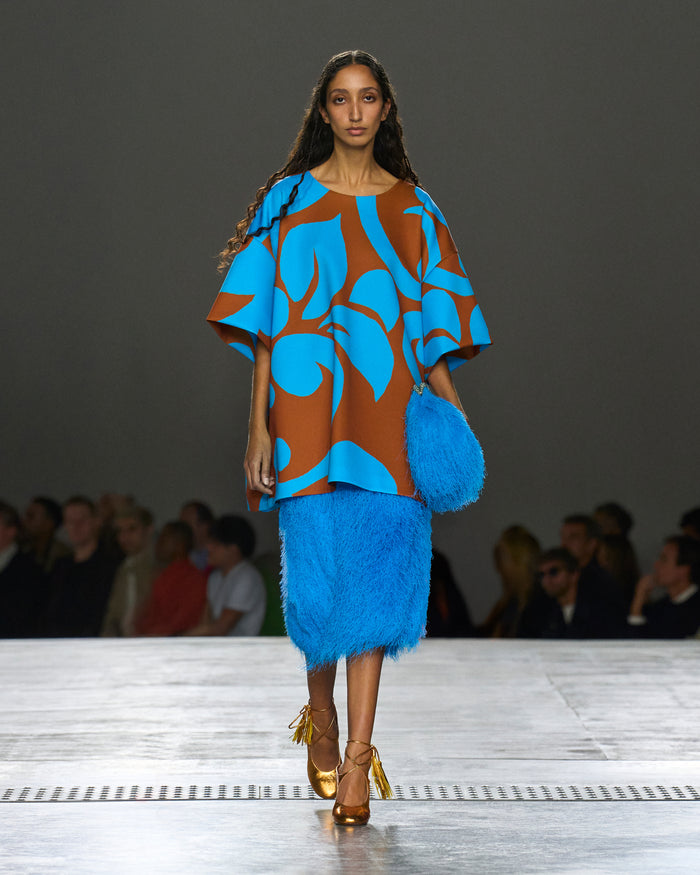 Model wearing a blue and brown outfit with feathered skirt on a runway.