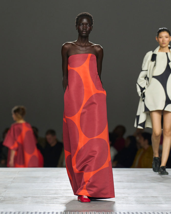 Model wearing a red and orange patterned dress on a fashion runway.