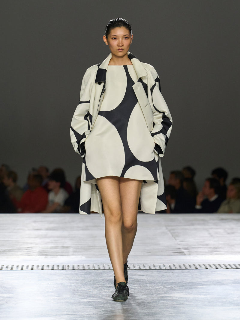 Model walking on a runway wearing a black and white patterned outfit.