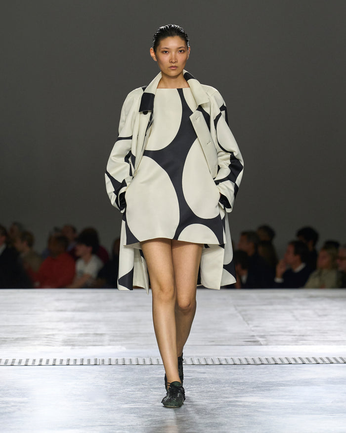 Model walking on a runway wearing a black and white patterned outfit.