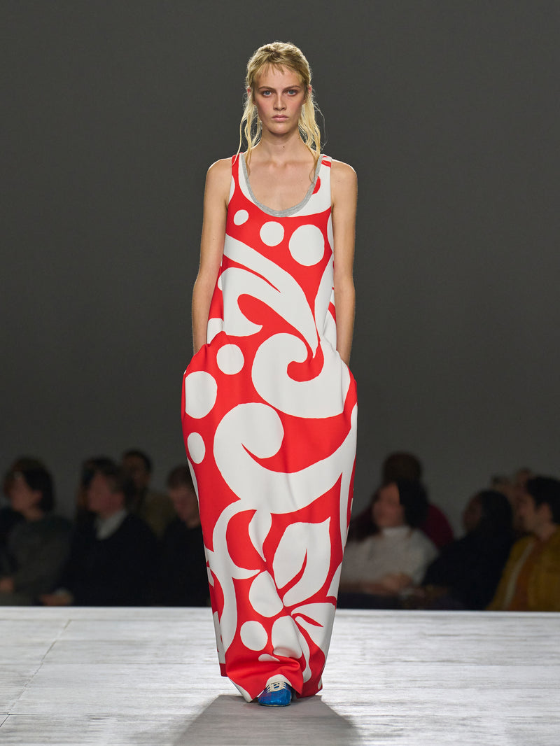 Model wearing a red and white patterned dress on a runway with an audience.