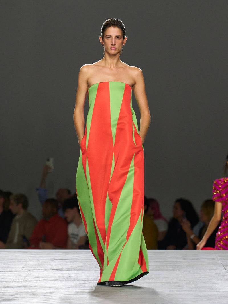 Model wearing a strapless dress with red and green vertical stripes on a runway.