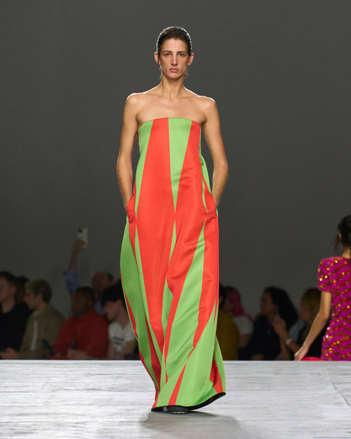 Model wearing a strapless dress with red and green vertical stripes on a runway.