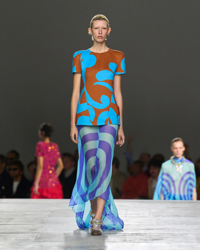 Model walking on a runway wearing a colorful outfit with abstract patterns.