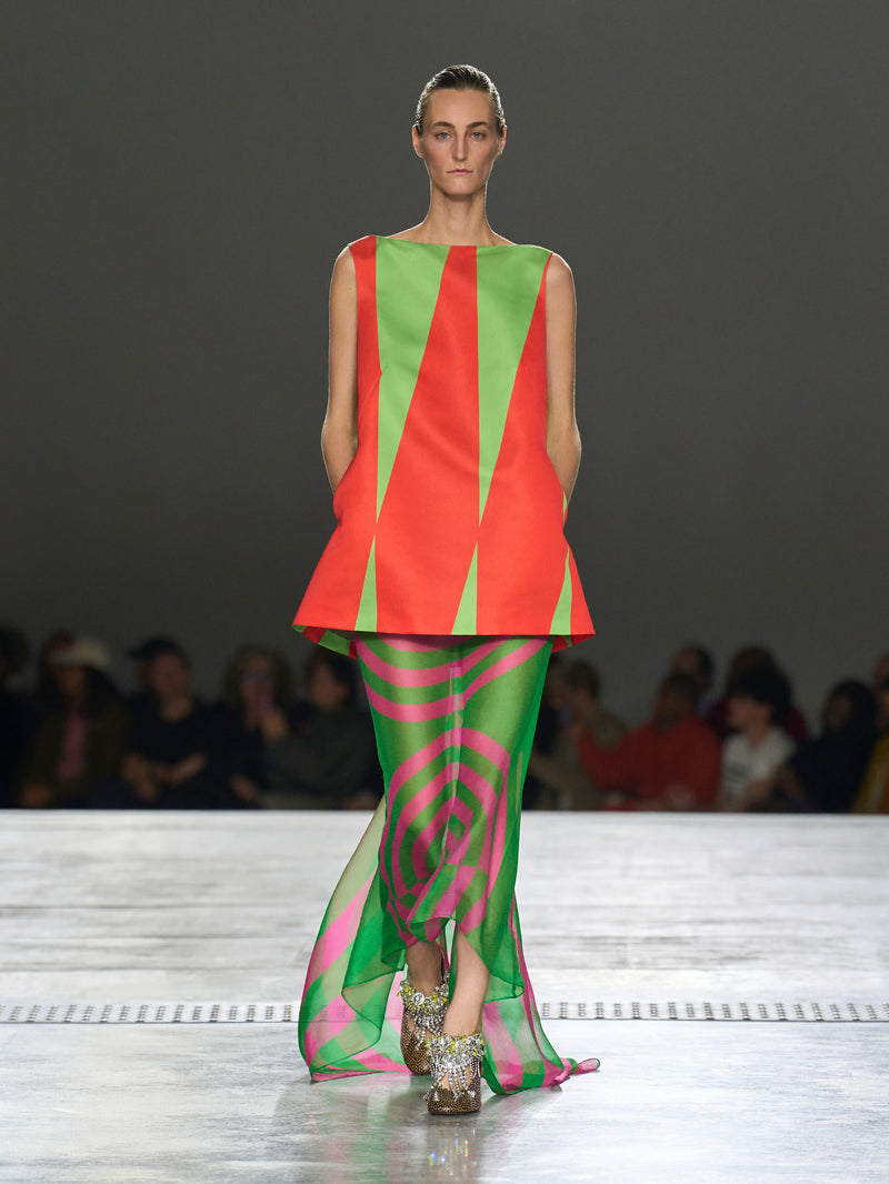 Model walking on a runway wearing a colorful outfit with geometric patterns.
