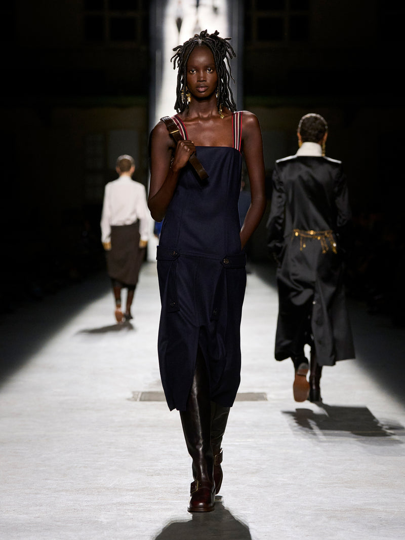 Model walking on a runway wearing a dark outfit with a blurred background