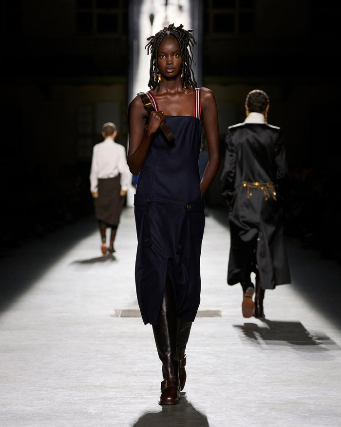 Model walking on a runway wearing a dark outfit with a blurred background