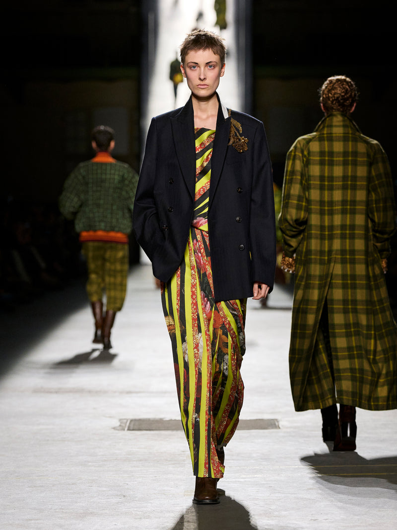 Model walking on a runway wearing a colorful outfit with a dark jacket.