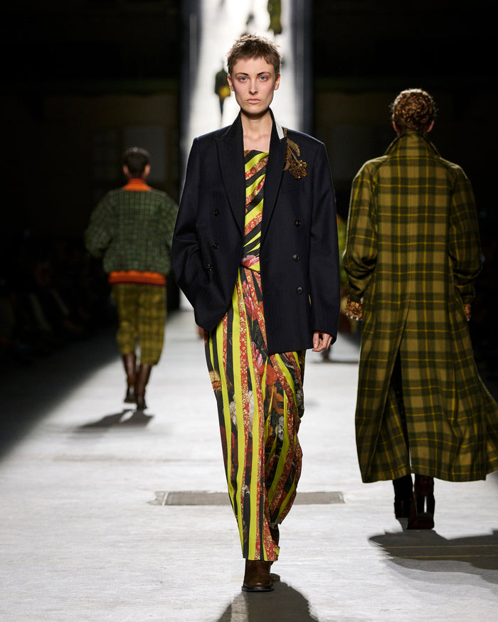 Model walking on a runway wearing a colorful outfit with a dark jacket.