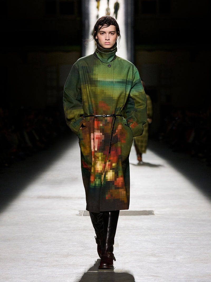 Model walking on a runway wearing a long, patterned coat.