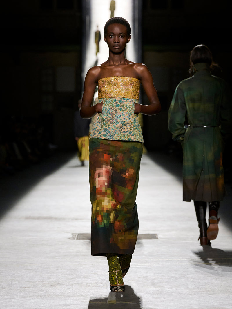 Model walking on a runway wearing a colorful outfit with abstract patterns.