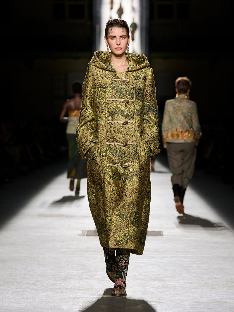 Model walking on a runway wearing a long, patterned coat.