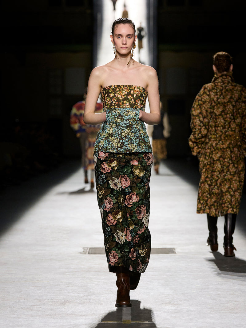 Model walking on a runway wearing a floral strapless dress.