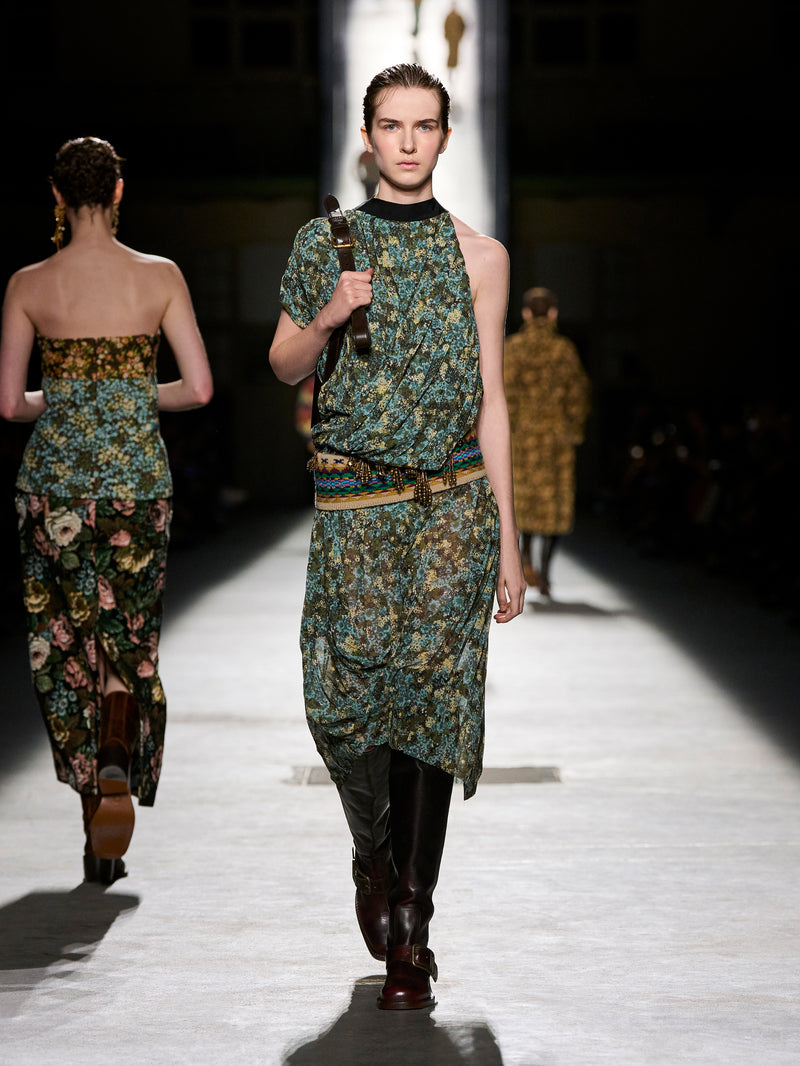 Model walking on a runway wearing a patterned outfit with floral designs.
