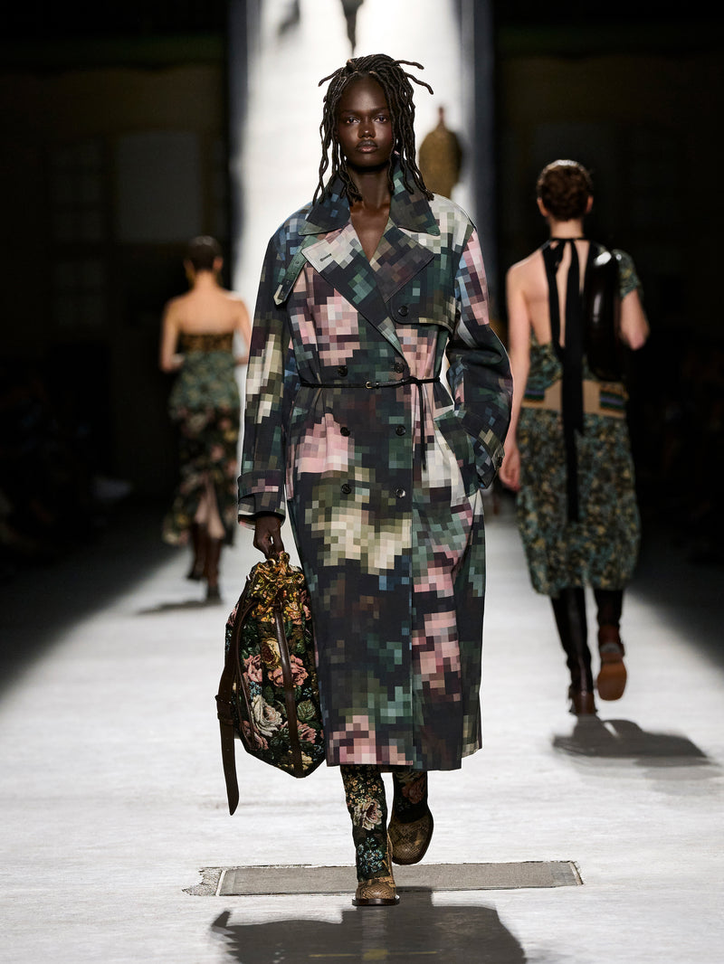 Model walking on a runway wearing a colorful, patterned outfit with a handbag.