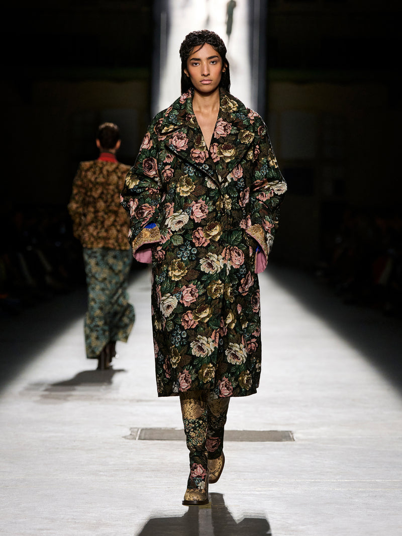 Model walking on a runway wearing a floral coat and pants.