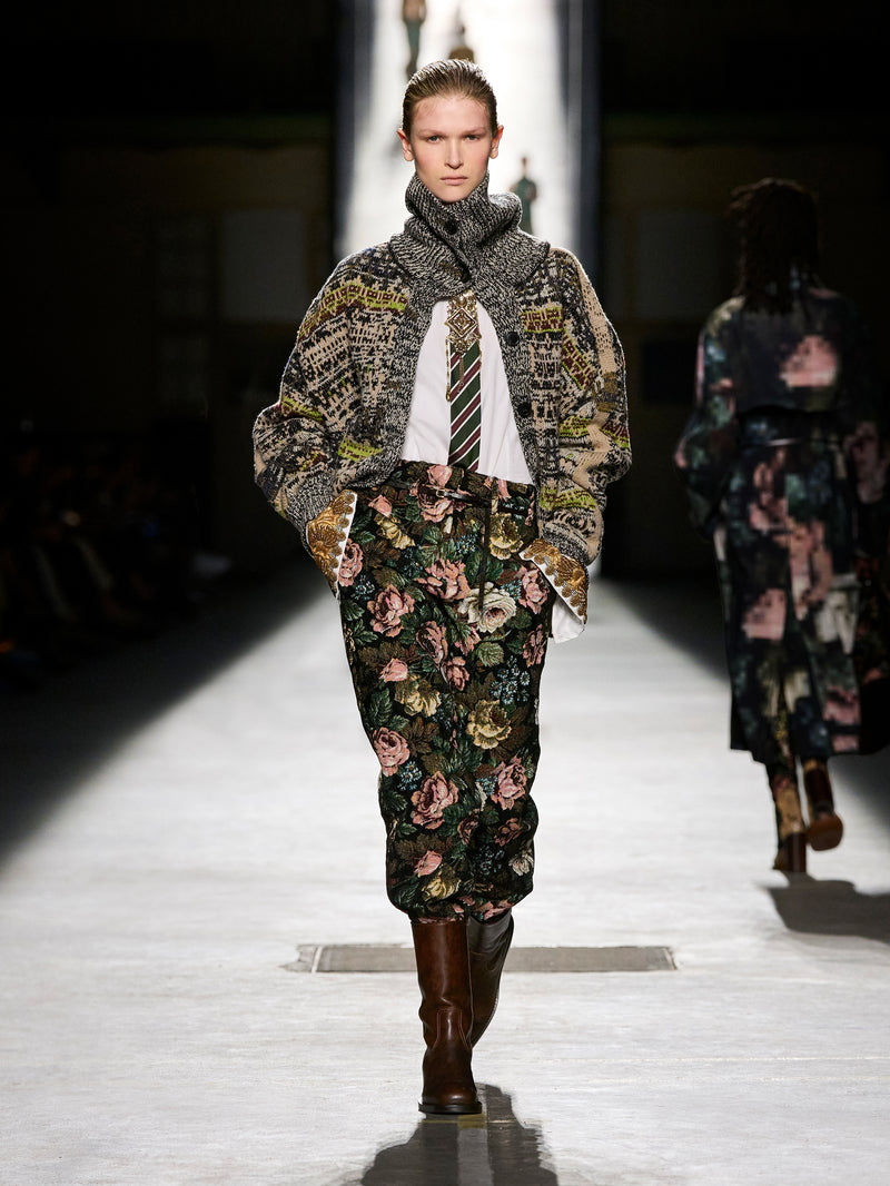 Model walking on a runway wearing a floral dress and patterned coat.