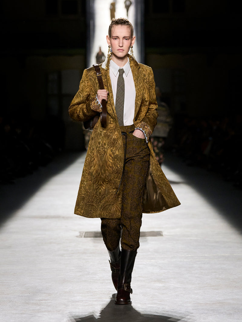 Model walking on a runway wearing a patterned coat and pants.