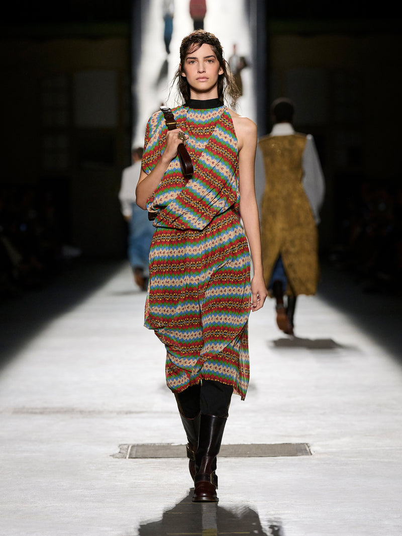Model walking on a runway wearing a colorful patterned dress.