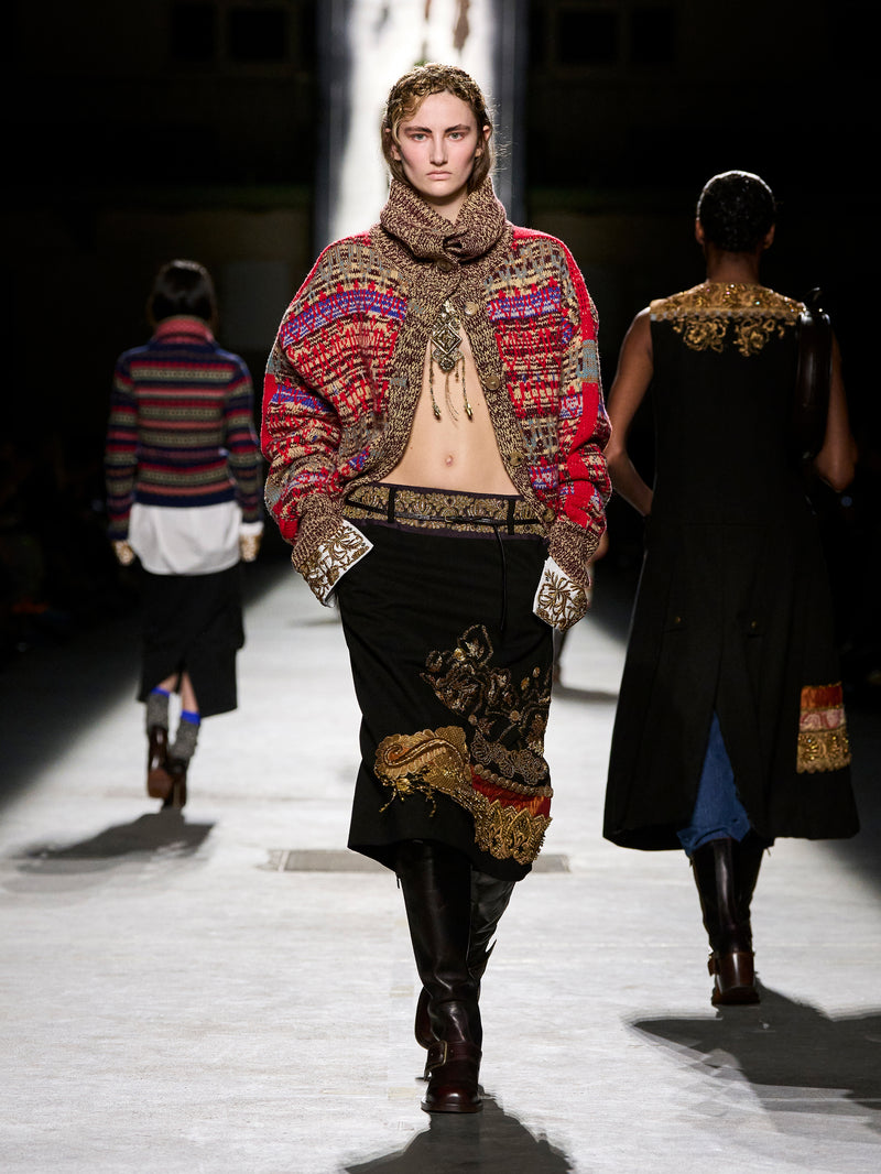 Model walking on a runway wearing a colorful, patterned outfit with a hood.