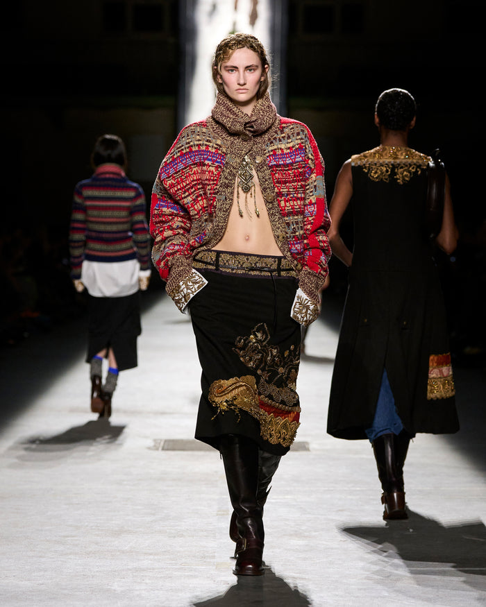 Model walking on a runway wearing a colorful, patterned outfit with a hood.