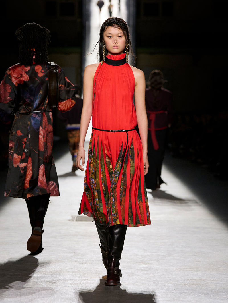Model walking on a runway wearing a red and patterned outfit.