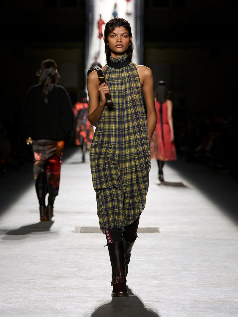 Model walking on a runway wearing a plaid dress and black boots.