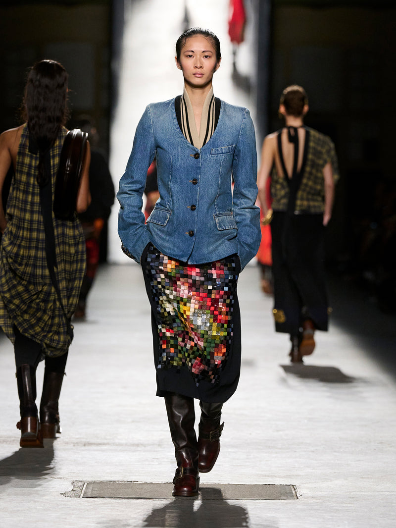 Model walking on a fashion runway wearing a denim jacket and colorful skirt.