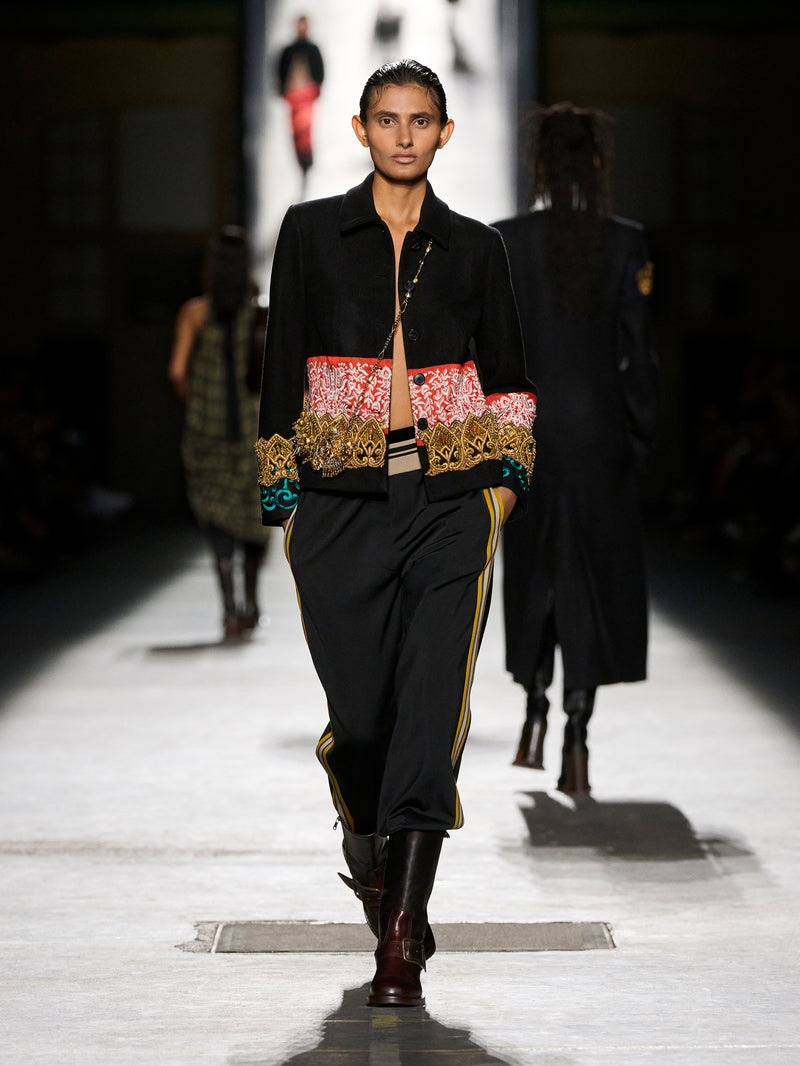 Model walking on a runway wearing a black outfit with colorful patterns.