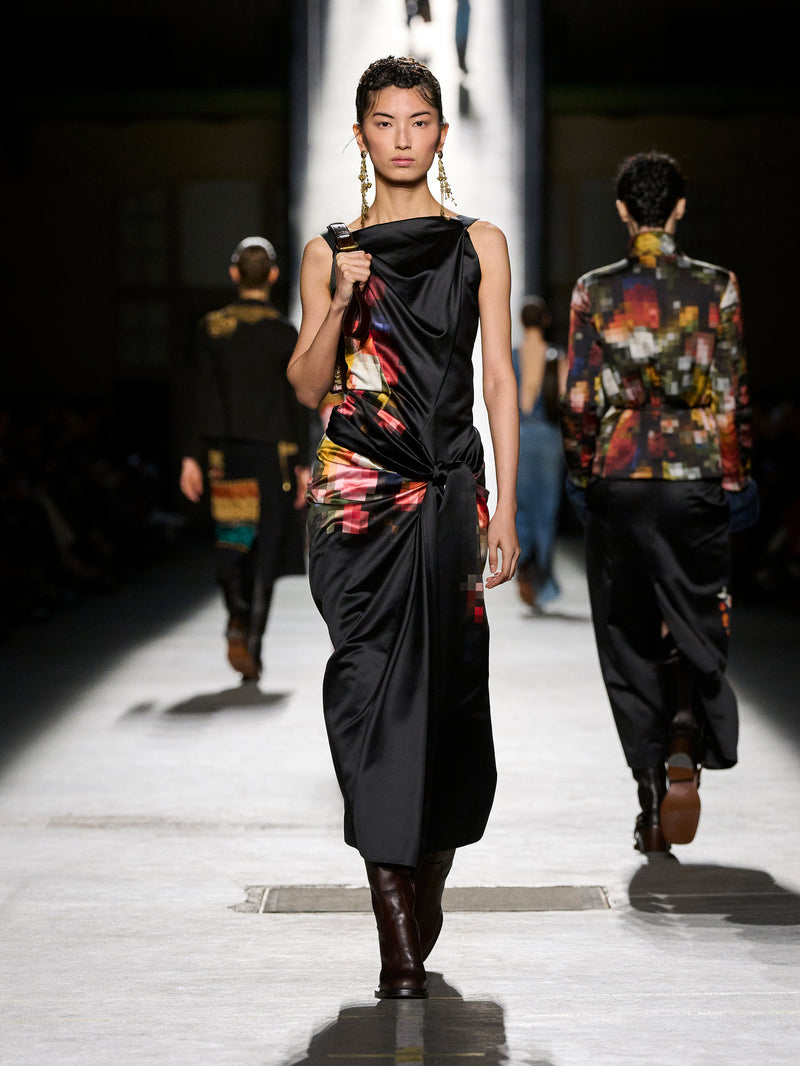 Model walking on a runway wearing a black dress with colorful patterns.