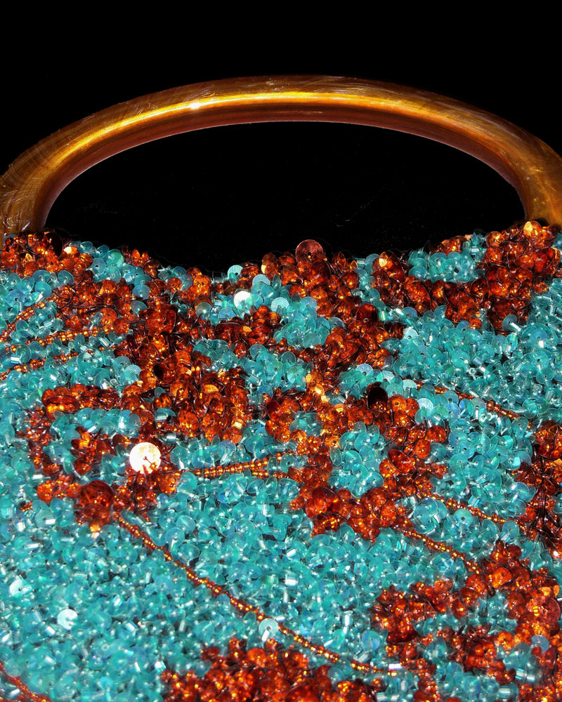 A close-up of a decorative handbag with blue and red embellishments on a black background