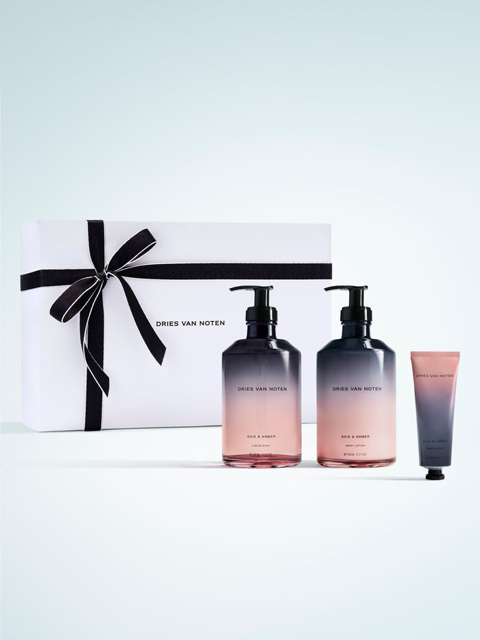 Dries Van Noten gift set featuring two gradient glass liquid soap and body lotion bottles and a matching hand cream, presented beside a white box with a black ribbon on a white background