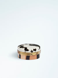 Closed round lip balm compact with a lid featuring black abstract floral motifs, gold-tone trim and a striped beige and black case