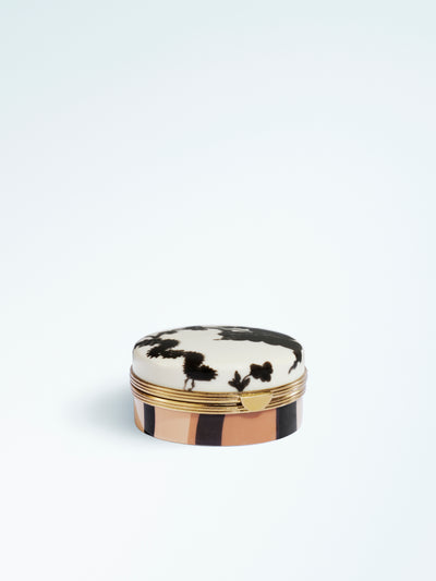Closed round lip balm compact with a lid featuring black abstract floral motifs, gold-tone trim and a striped beige and black case