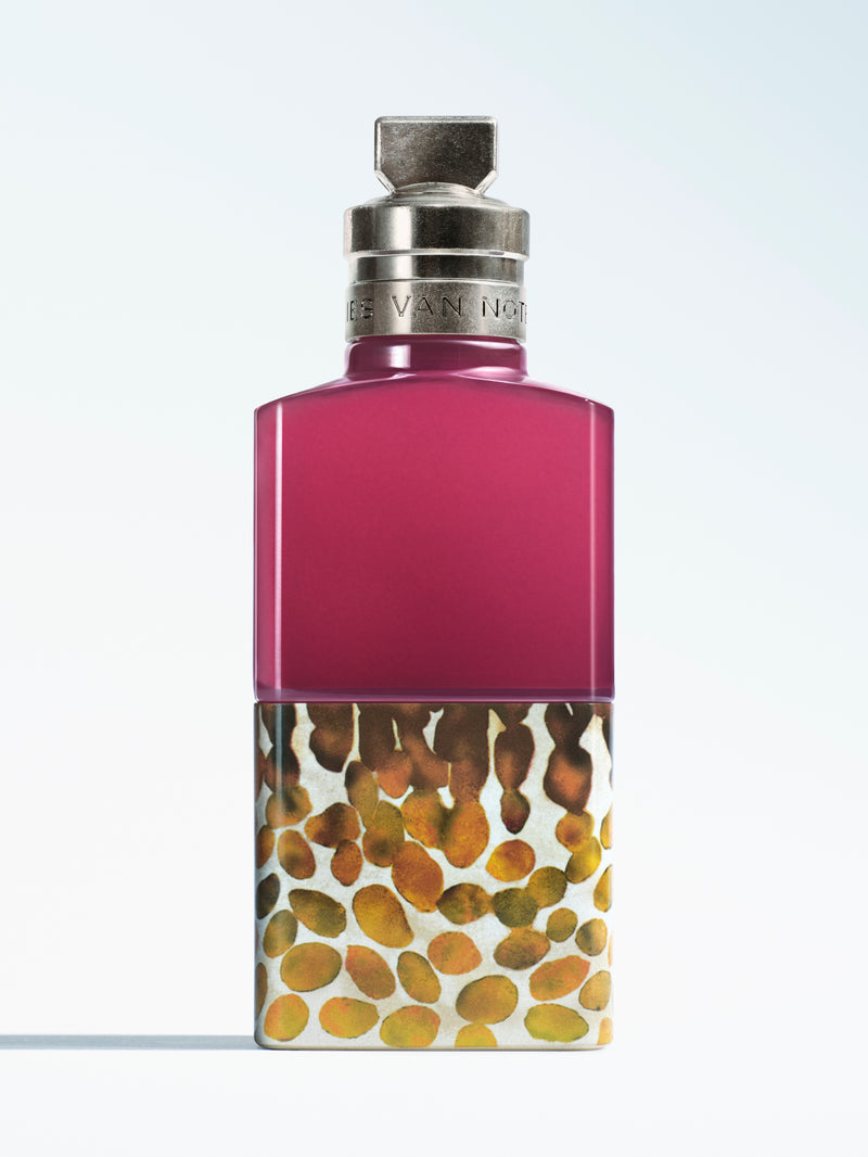 A perfume bottle with a magenta-pink upper section and a lower section featuring a gold, brown, and beige spotted pattern, topped with a silver cap