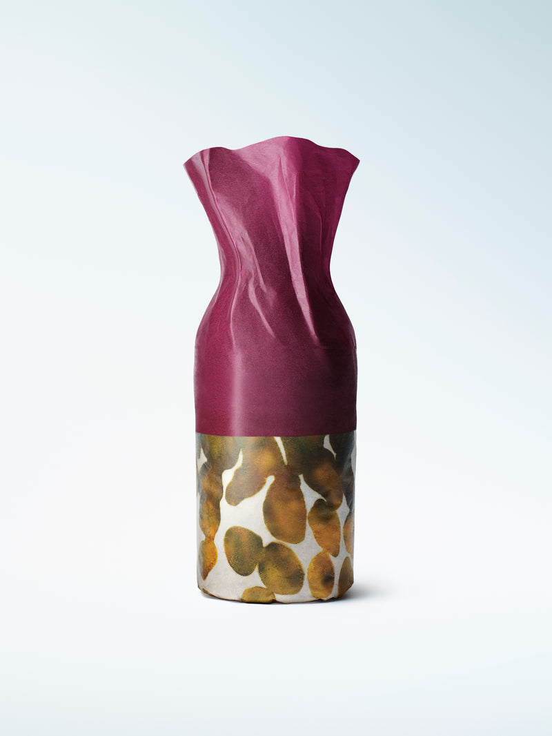 A refillable perfume bottle with a sculptural deep magenta top and cylindrical base decorated with a gold, brown, beige pattern.