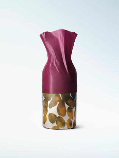 A refillable perfume bottle with a sculptural deep magenta top and cylindrical base decorated with a gold, brown, beige pattern.